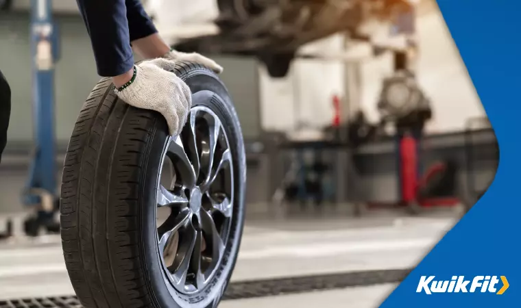 A technician wearing gloves rolls a spare tyre away.