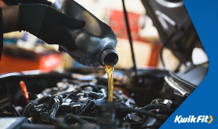 Technician wearing black gloves pouring oil into a car whilst the bonnet is up.